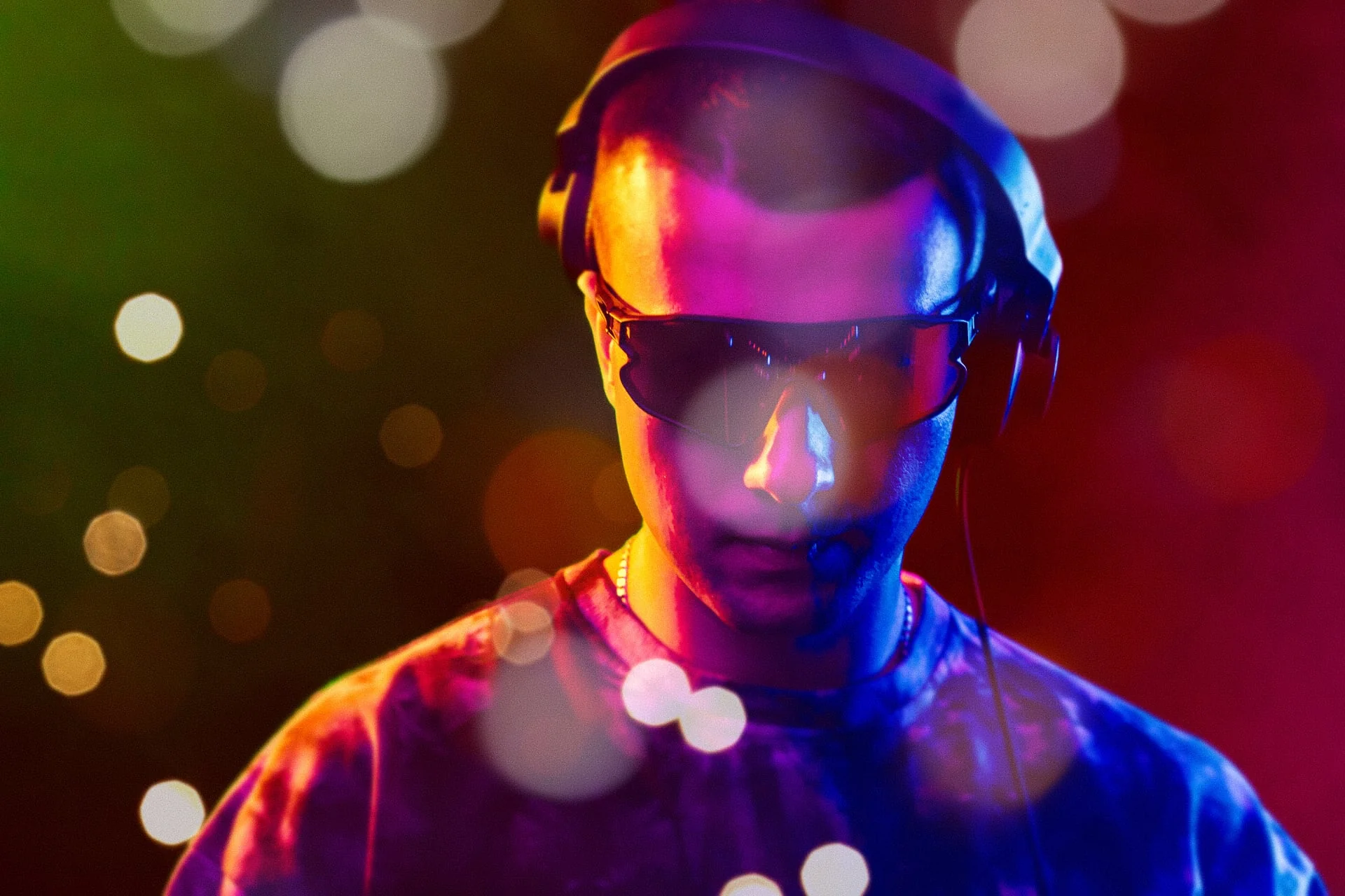EDM artist wearing headphones and futuristic sunglasses surrounded by colorful festival bokeh lights — Castella Media Group EDM music video promotion